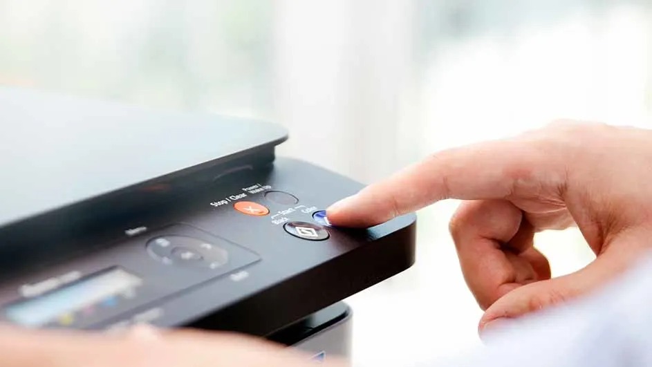 Vinger drukt op de blauwe kopieerknop van een zwarte all-in-one printer; bedieningspaneel met stop, zwart en kleur zichtbaar. 