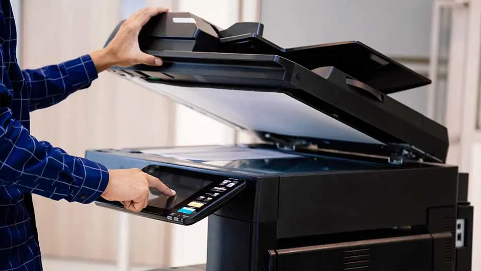 Een persoon bedient een zwart kantoorapparaat met een open deksel en een touchscreen.