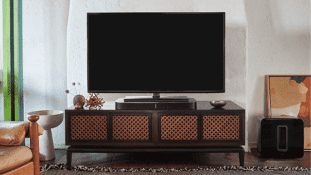 Zwarte tv op een kast met roodbruine details. Een witte stoel en een schilderij zijn ook zichtbaar.