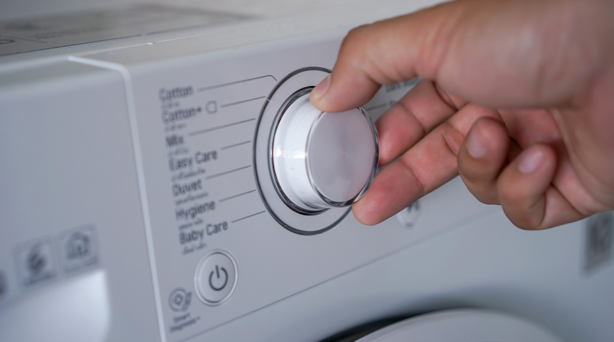 Een hand draait aan een knop op een witte wasmachine met verschillende wasprogramma's.