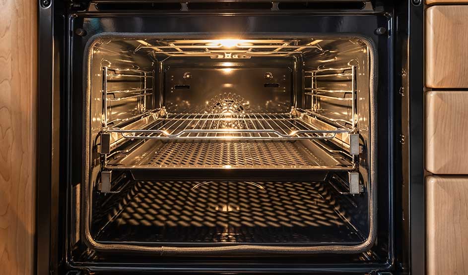 A clean, empty oven with shining racks and the light on stands open in a wooden kitchen unit.