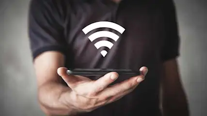 Een man houdt een zwarte telefoon vast met een wit wifi-symbool erboven, tegen een grijze achtergrond.