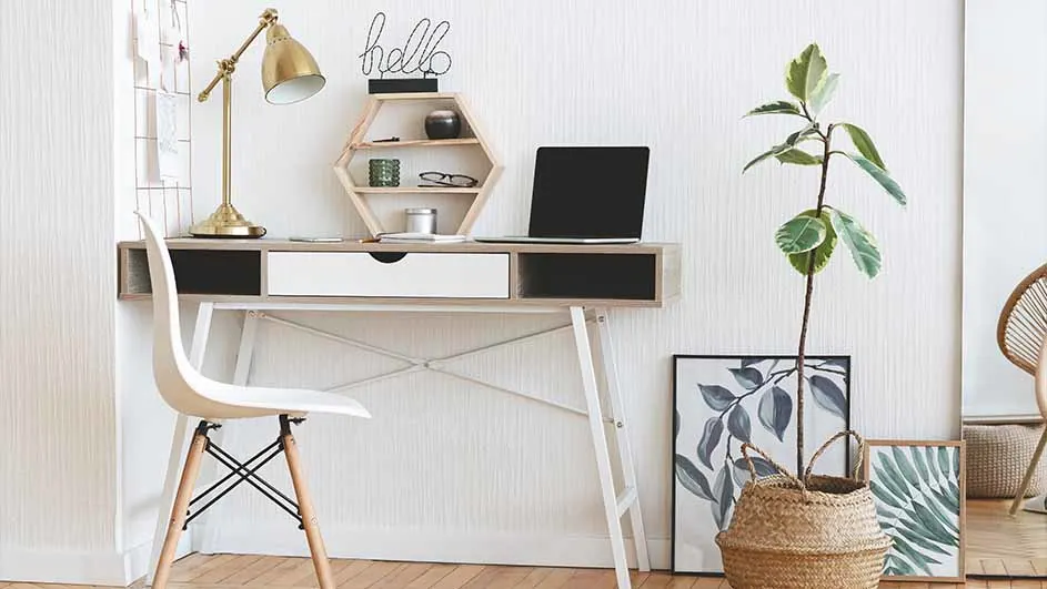 Bureau met laptop, lamp en zeshoekige plank aan de muur, met stoel, plant en decoratieve afbeeldingen op de vloer.