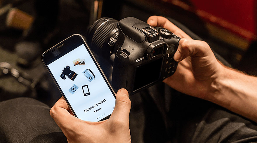 Een persoon houdt een zwarte Canon camera en een smartphone vast met de app 'Camera Connect' open.