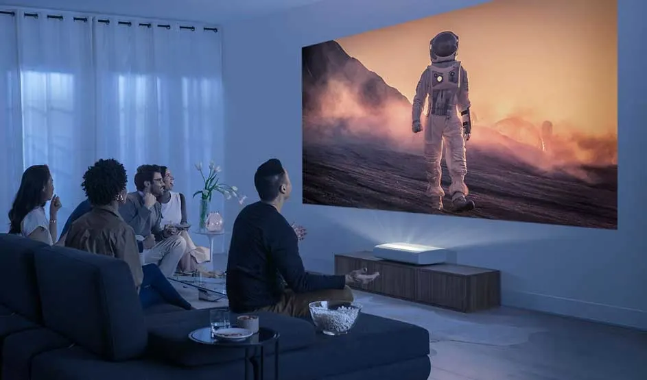 A group watch in a dark living room as a huge projection shows an astronaut on a distant planet.