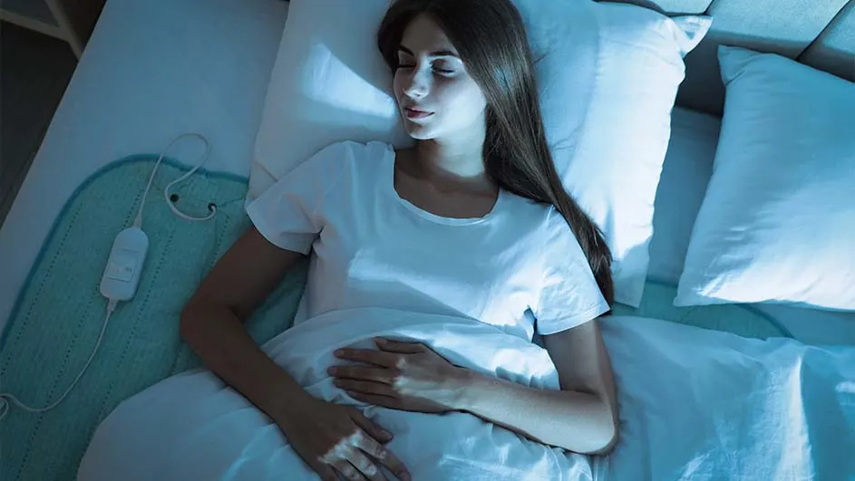 Een vrouw slaapt in een wit T-shirt op een wit kussen in bed onder een wit dekbed met een groene elektrische deken.