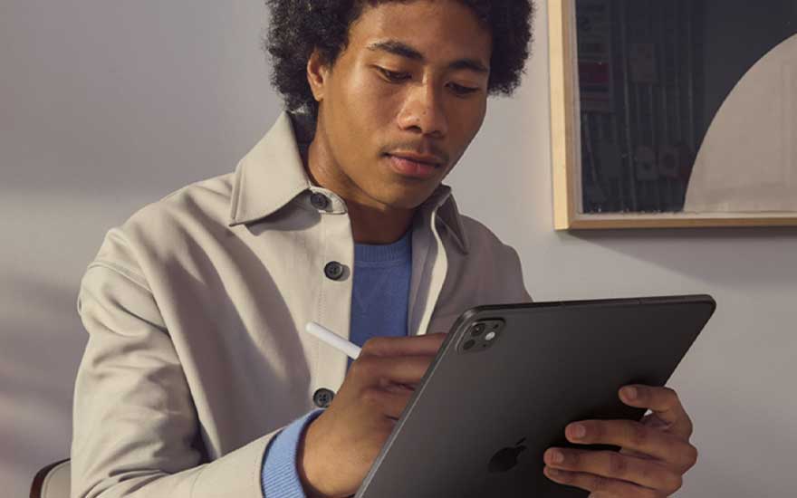 Man in a light jacket carefully writes with a stylus on a dark tablet at a table in a modern, minimalist indoor space.