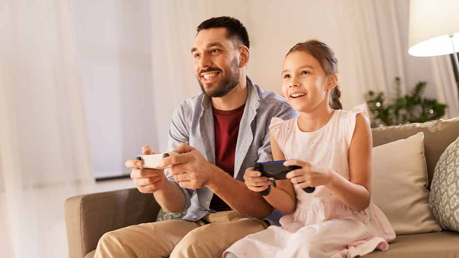 Een man en een meisje zitten op een bank en spelen videospelletjes met controllers in hun handen.