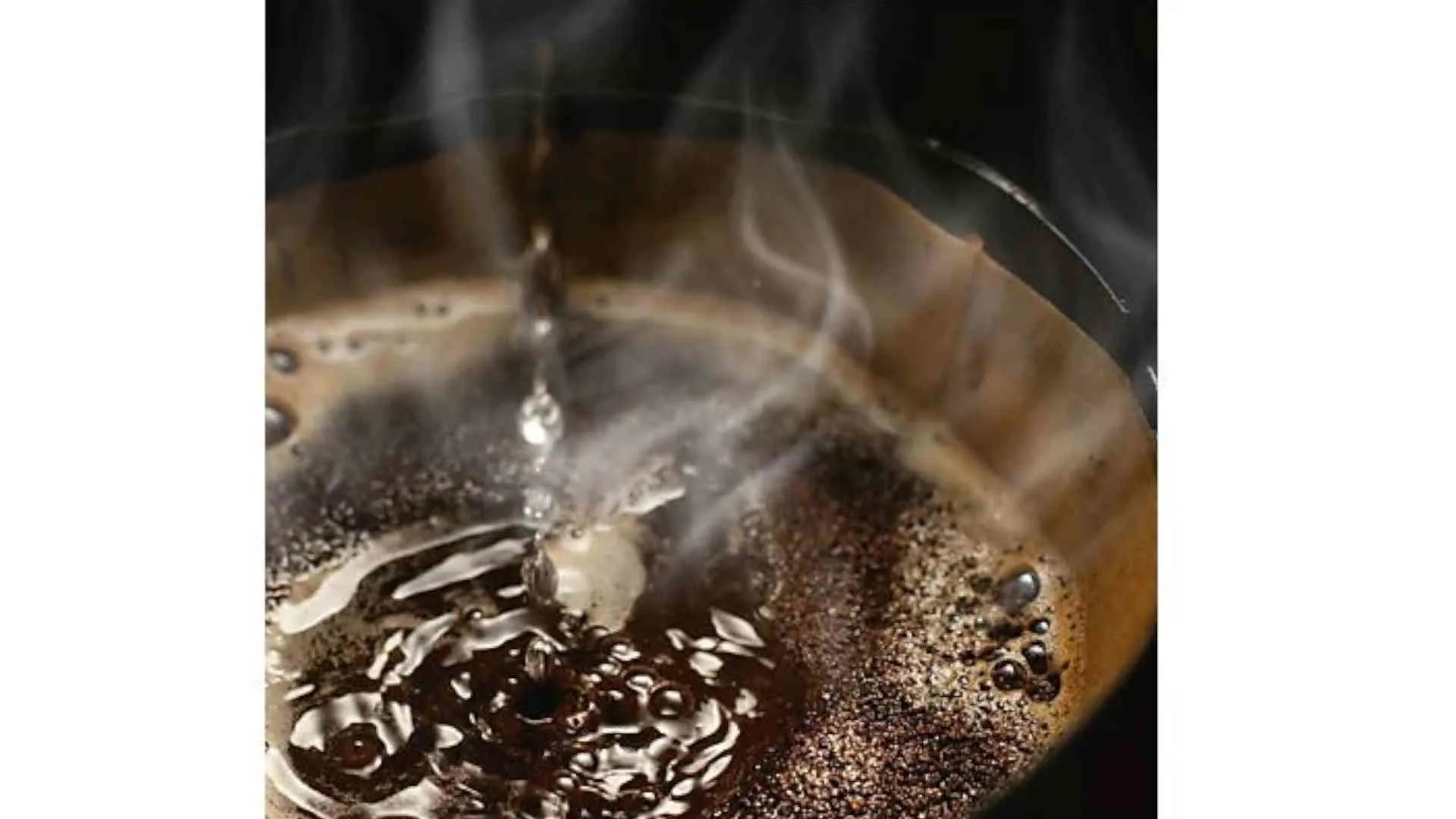 Een close-up van een kop koffie met stoom en een druppel die erin valt.