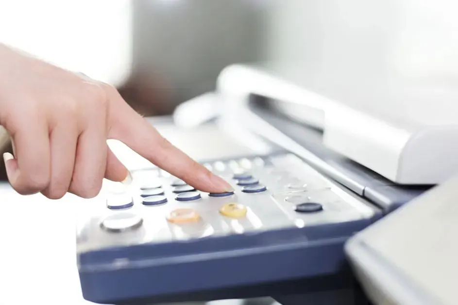 Een hand bedient de knoppen van een kopieerapparaat of printer in een kantooromgeving. Het merk van het apparaat is niet zichtbaar.