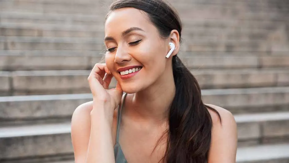 Jonge vrouw met een paardenstaart, draagt een wit oortje en glimlacht, zittend voor een trap.