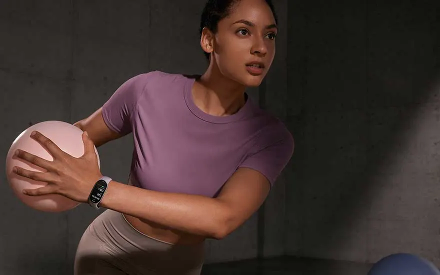 A person wearing a black fitness tracker on their left wrist holds a black smartphone in their right hand, outdoors.