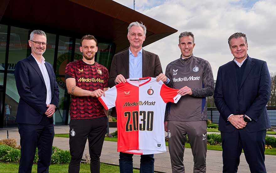 Vijf mannen poseren voor een stadion, twee in Feyenoordkleding, terwijl in het midden een speciaal MediaMarkt‑shirt met jaartal 2030 wordt getoond.