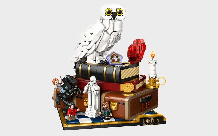 LEGO Harry Potter-display met witte uil op boeken, tovervoorwerpen, koffer, kaars en kleine figuren op een elegante basis.