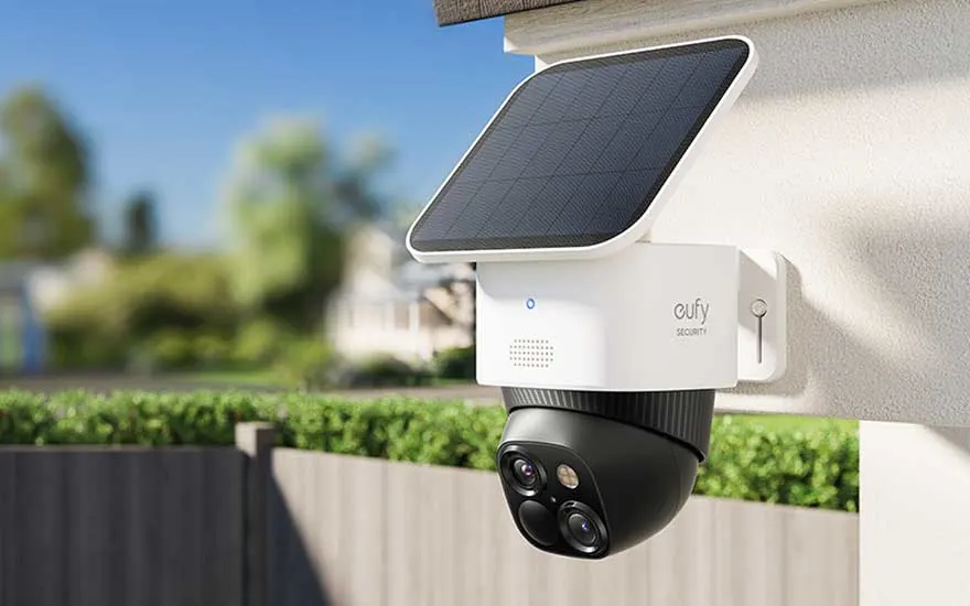 Een zwarte en witte Eufy bewakingscamera met zonnepaneel is aan een witte muur bevestigd.