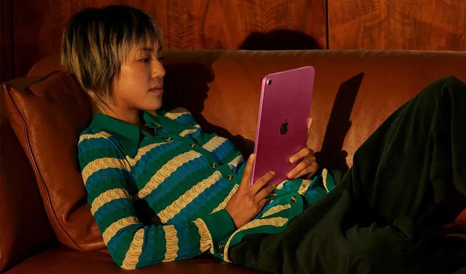 Iemand ligt ontspannen op een bruine bank en houdt een paarse Apple iPad vast. De achtergrond bestaat uit een houten wand.