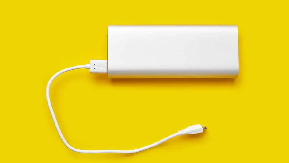Een witte powerbank ligt op een gele achtergrond, met een witte kabel aangesloten.