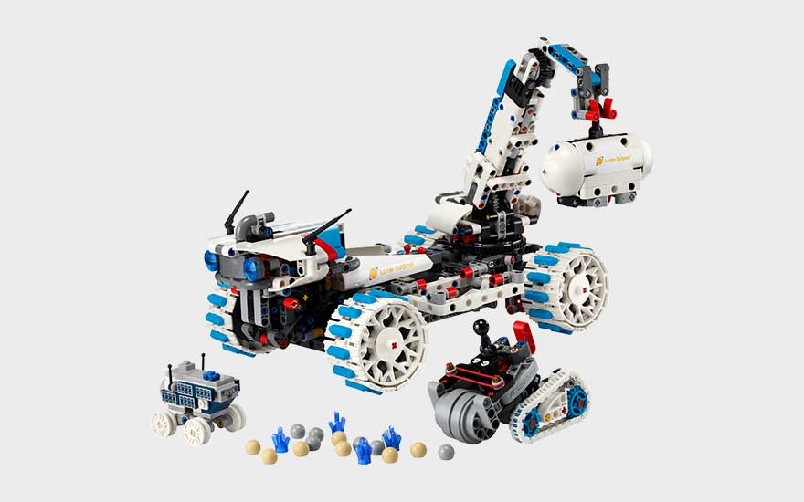 Witte LEGO ruimterover met kraanarm, grote wielen, kleine voertuigen en accessoires voor een maanmissie op grijze achtergrond.
