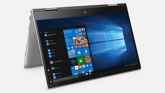 Een zilverkleurige laptop staat open met het Windows-startscherm op een witte achtergrond. Het scherm toont applicatiepictogrammen.