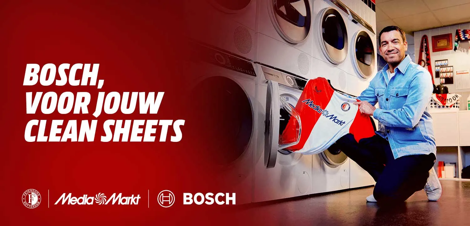 Giovanni van Bronckhorst gehurkt bij een wasmachine met een Feyenoord-shirt in zijn hand.