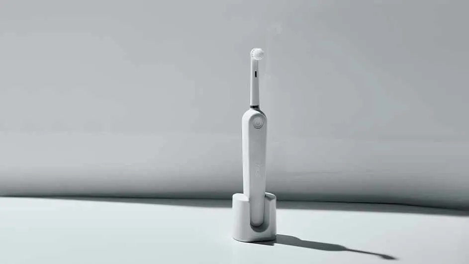 Een witte elektrische tandenborstel staat in een witte houder tegen een witte achtergrond.