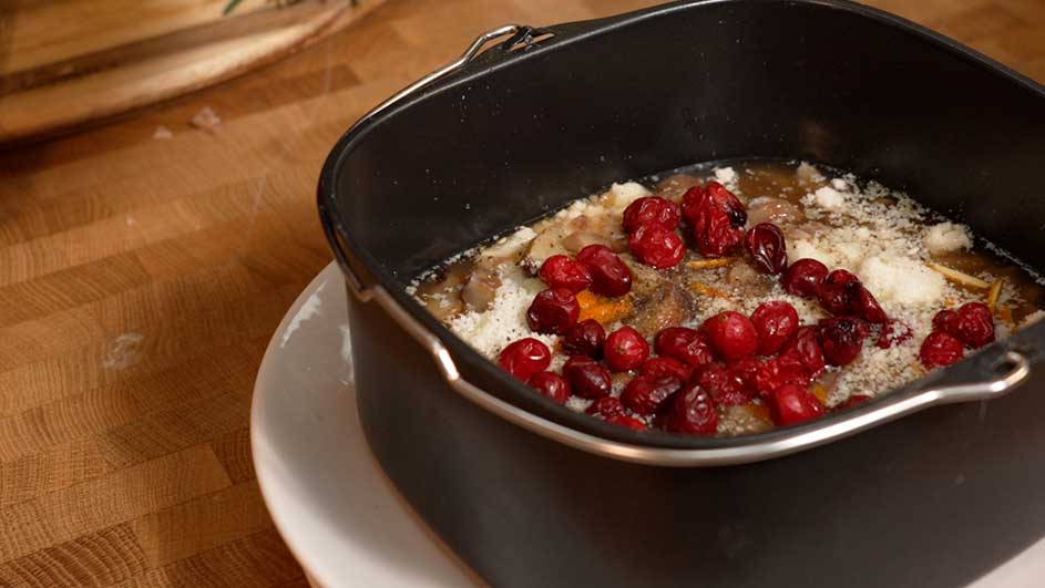 Ovenschaal met vlees, saus, geraspte kaas en verse rode bessen op een houten aanrecht.