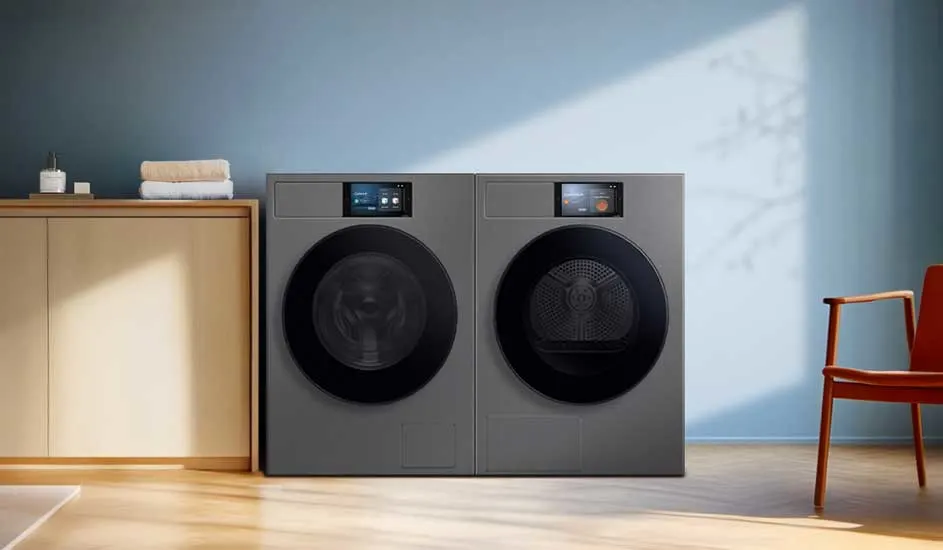 Moderne wasruimte met twee grijze frontloaders naast elkaar, bovenop digitale displays; links kast met handdoeken, rechts een houten stoel.