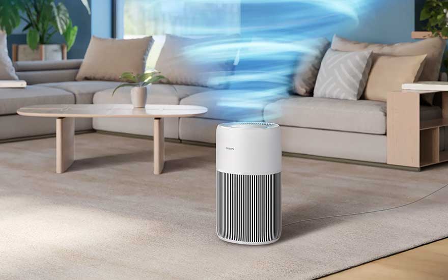 In een lichte woonkamer blaast een witte Philips luchtreiniger een draaiende blauwe luchtwervel omhoog naast een moderne beige hoekbank.