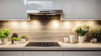 Keuken met grijze kasten, een rvs afzuigkap, een zwarte kookplaat en planten en bloemen in witte potten.