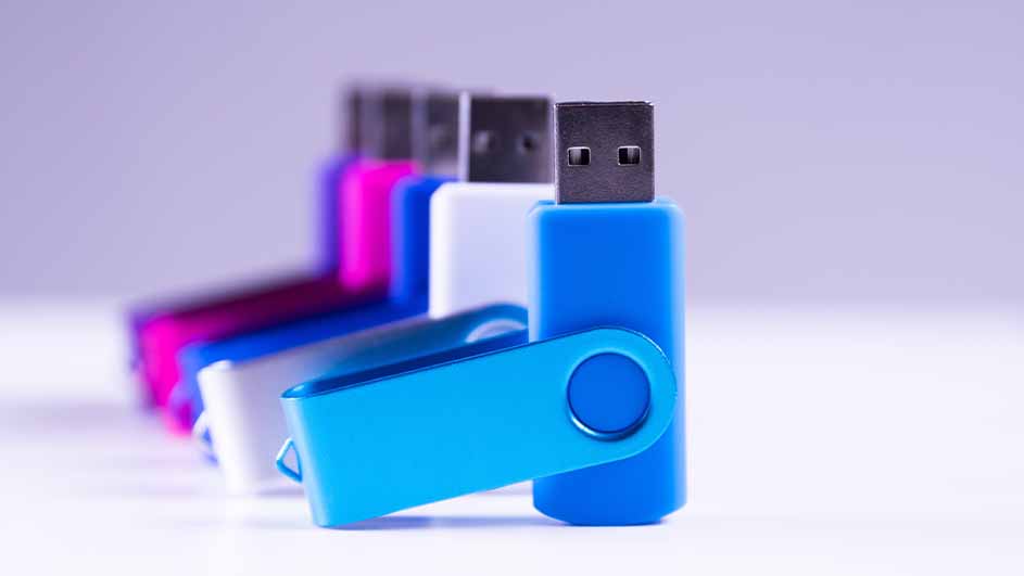 Rij van USB-sticks in diverse kleuren, waaronder blauw, wit en roze, tegen een lichte achtergrond.