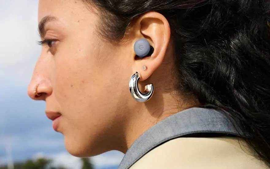 Een vrouw draagt Pixel Buds in haar oor, met een opvallende zilveren oorbel ernaast, buiten in natuurlijk daglicht.