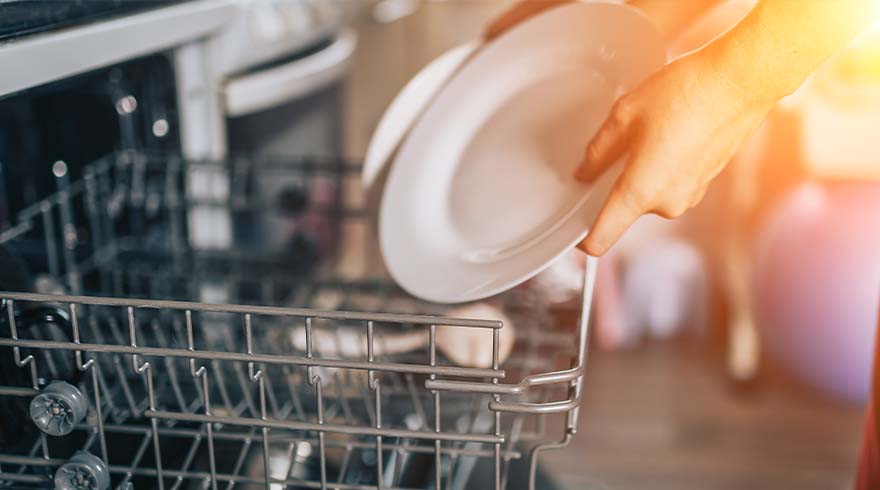 Iemand plaatst een wit bord in een openstaande vaatwasser met een metalen rek.