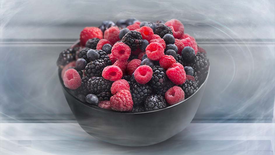 Een zwarte kom gevuld met frambozen, bramen en blauwe bessen tegen een vage achtergrond.