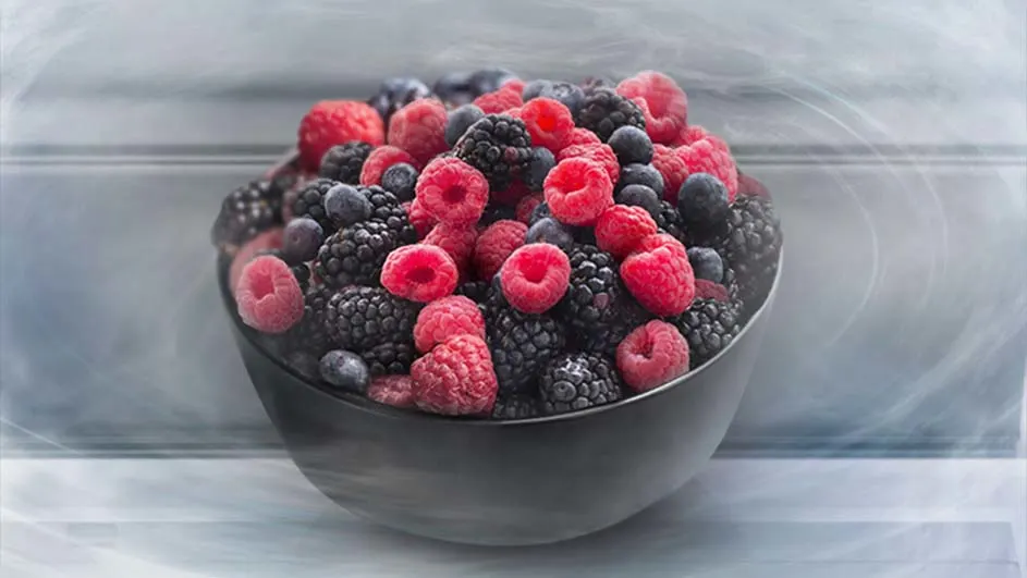 Een zwarte kom gevuld met frambozen, bramen en blauwe bessen tegen een vage achtergrond.
