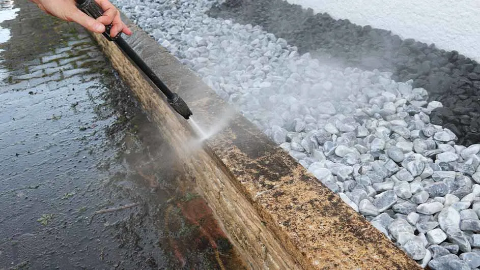 Persoon gebruikt een hogedrukreiniger om een lage tuinmuur schoon te maken naast decoratieve witte en zwarte stenen.