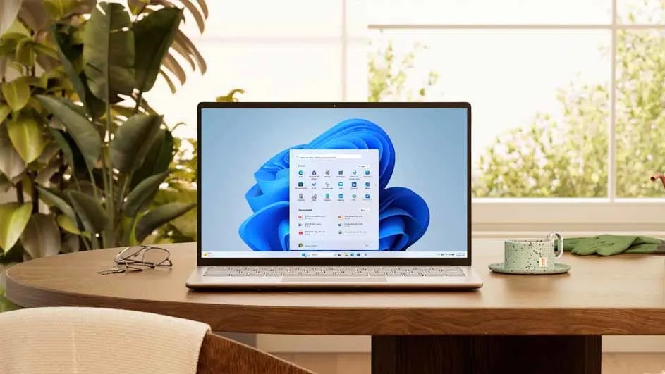 Op een houten tafel staat een open HP laptop met Windows 11, naast een bril en een groene mok. Merknaam: HP.