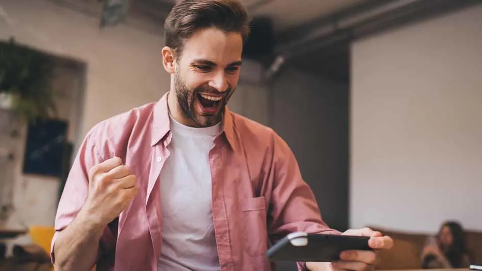 Een man in een roze overhemd kijkt naar een tablet en balt zijn vuist van vreugde.