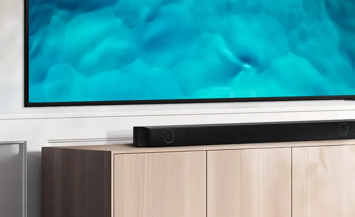 Een tv met blauwe afbeeldingen hangt boven een houten kast. Een zwarte soundbar staat op de kast.
