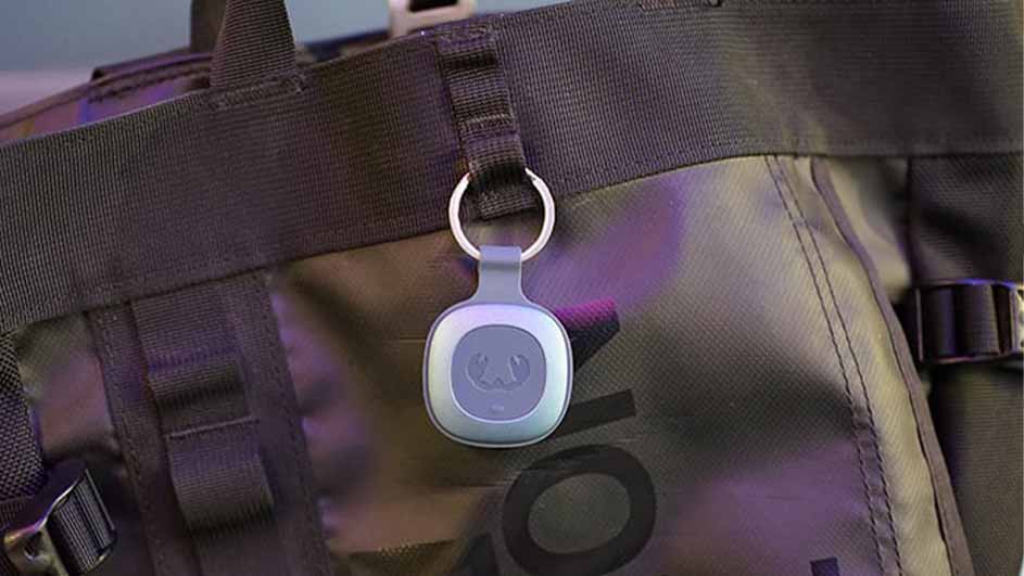 Een grijze bagagelabel met een ring hangt aan een zwarte tas met riemen en een logo.