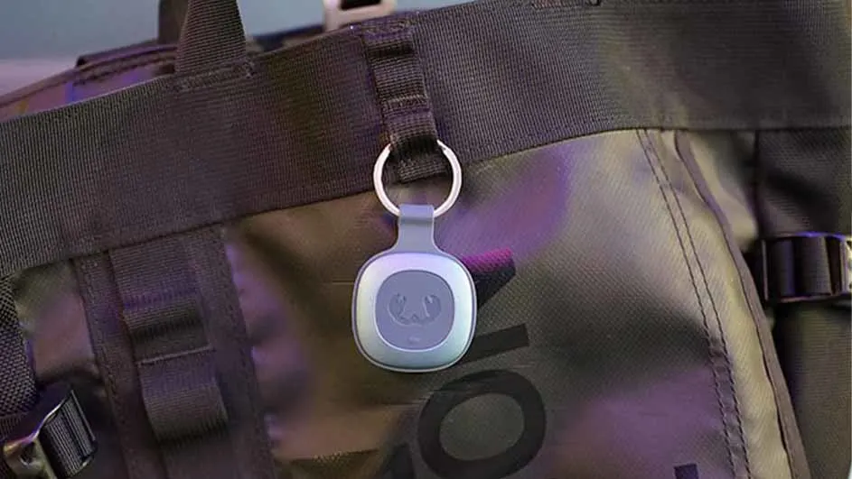 Een grijze bagagelabel met een ring hangt aan een zwarte tas met riemen en een logo.