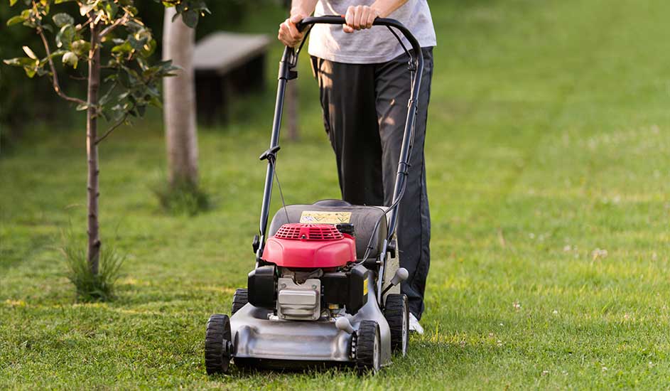 Een persoon maait het gras met een rood-zilveren grasmaaier in de tuin. Het merk van de grasmaaier is niet zichtbaar op de foto.