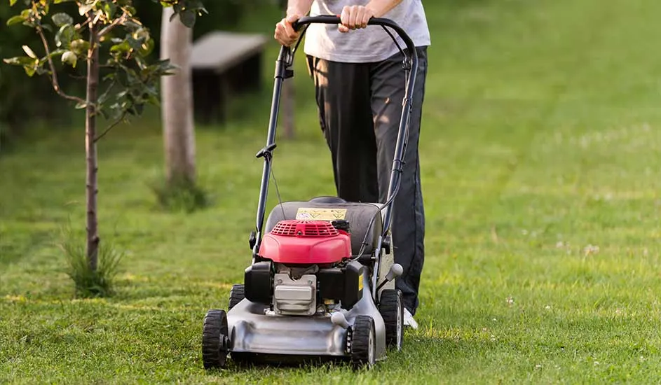 Een persoon maait het gras met een rood-zilveren grasmaaier in de tuin. Het merk van de grasmaaier is niet zichtbaar op de foto.