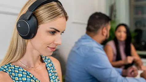 Jonge vrouw met grote koptelefoon werkt geconcentreerd aan haar bureau, terwijl twee collega’s op de achtergrond samen overleggen.
