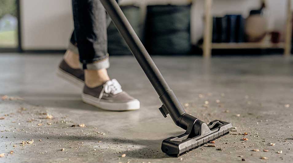 Iemand stofzuigt de vloer met een Kärcher stofzuiger, waarbij vuil en stof zichtbaar worden opgezogen.