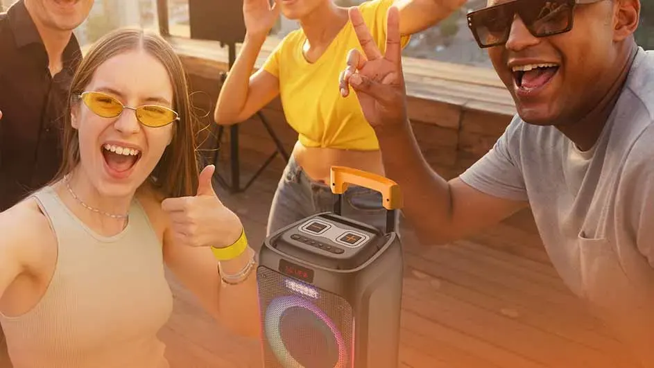 Een groep mensen lacht en danst rond een draagbare luidspreker met gekleurde lichten.