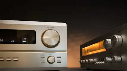 Two silver audio receivers with dials and buttons, one showing CD and volume output against a dark background.