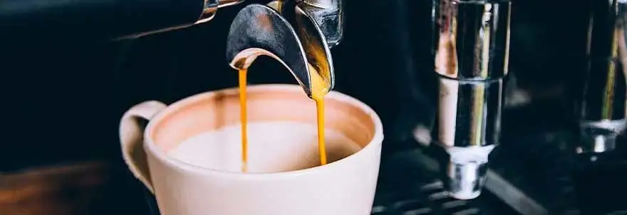 Espresso stroomt uit een zilverkleurige machine in een witte mok, op een donkere achtergrond.