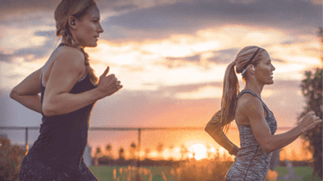Twee vrouwen in sportkleding rennen buiten met bomen en een zonsondergang op de achtergrond.