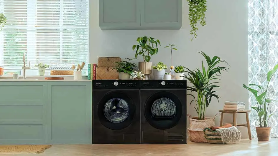 Wasmachine en droger naast elkaar in een lichte ruimte met planten en houten accenten.