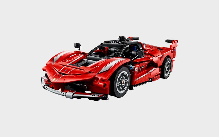 Rode LEGO Ferrari-racewagen met witte strepen, grote spoiler, sportieve lijnen en gedetailleerde cockpit op grijze achtergrond.